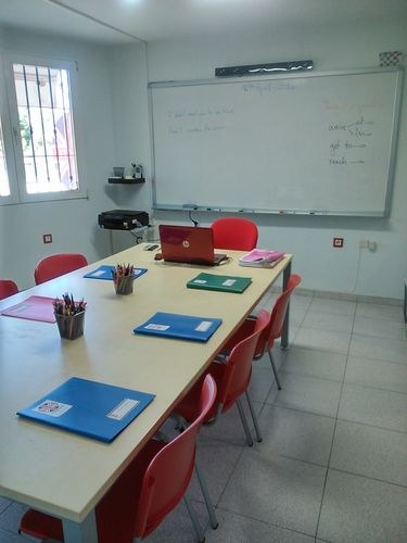 Aula Brisbane con mesa central, pizarra y material de clase